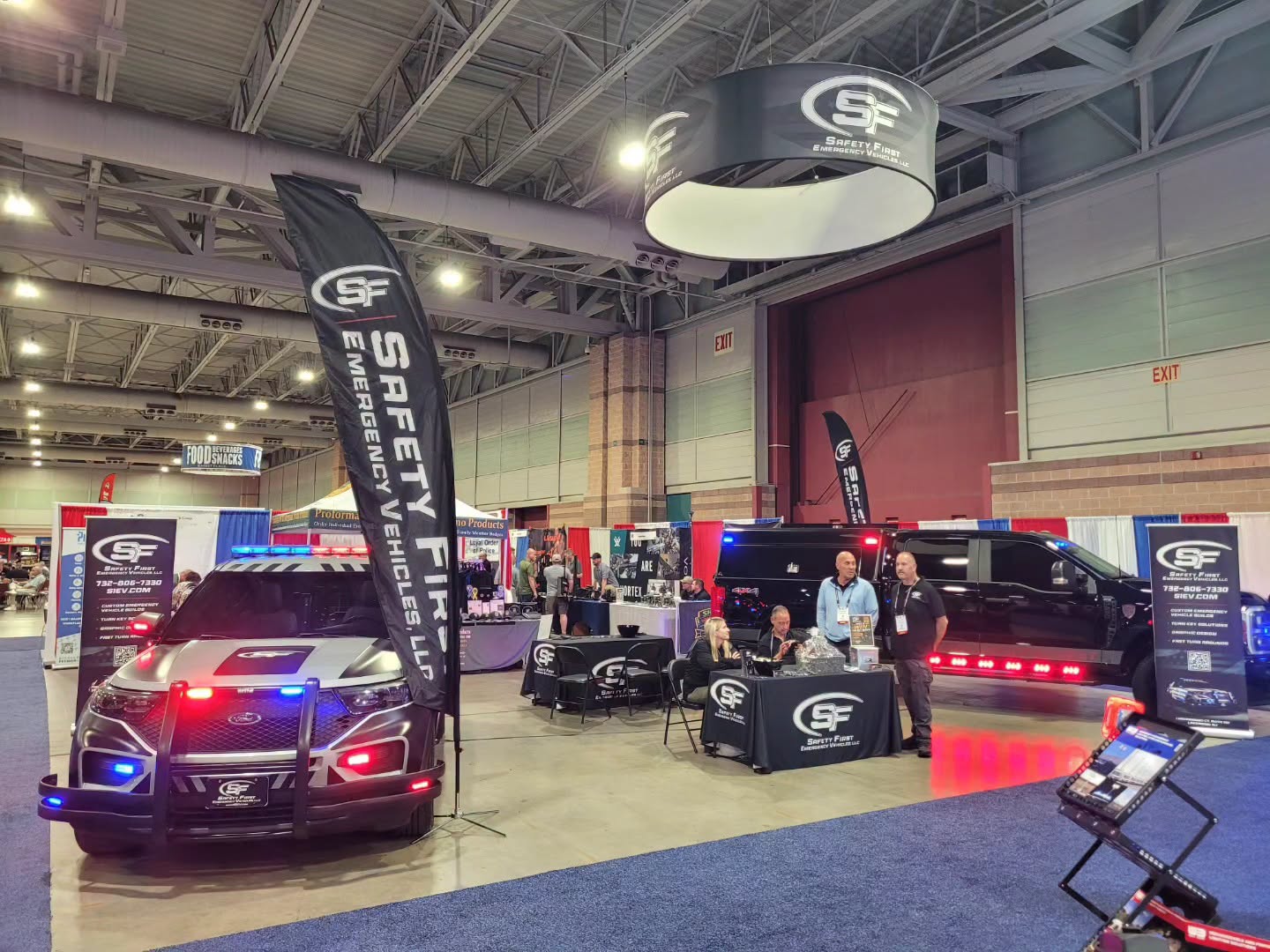 The SafetyFirst Emergency Vehicles booth at the 2026 Police Security Expo, with a lit Ford Police Interceptor Utility, branded feather flags, and a custom Ford Super Duty.
