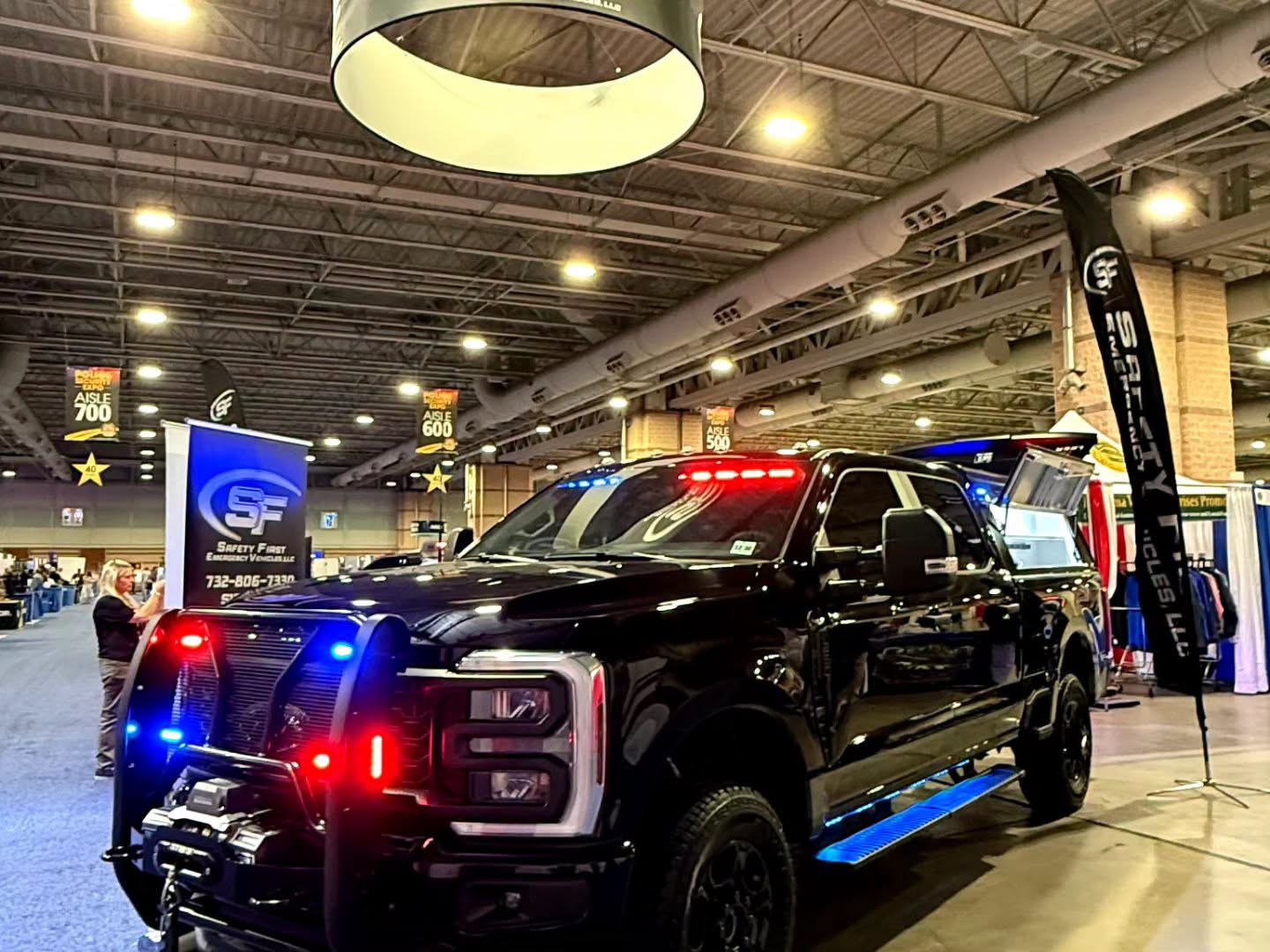 Three-quarter front view of the custom Ford Super Duty demo truck under the SafetyFirst hanging banner.
