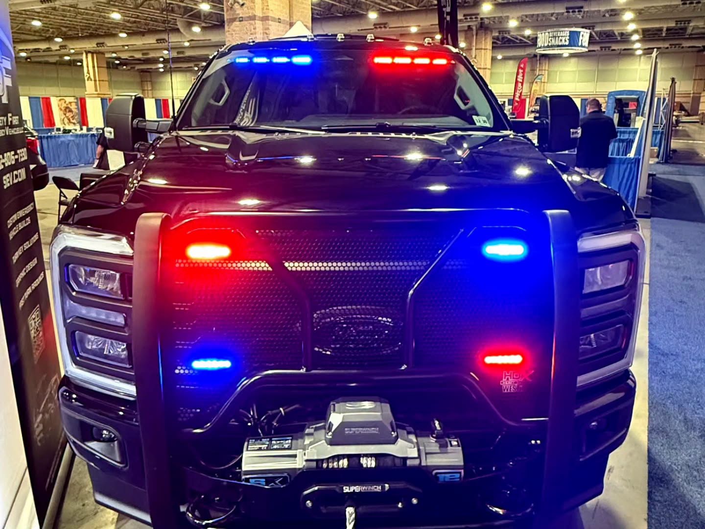 Front view of a blacked-out Ford Super Duty with push bumper, winch, and red and blue warning lights at the SafetyFirst booth.